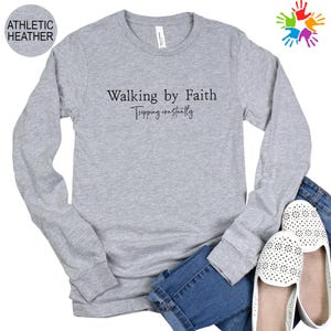 a gray long-sleeved shirt with the text "Walking by Faith" printed on it, along with a pair of jeans and white shoes.