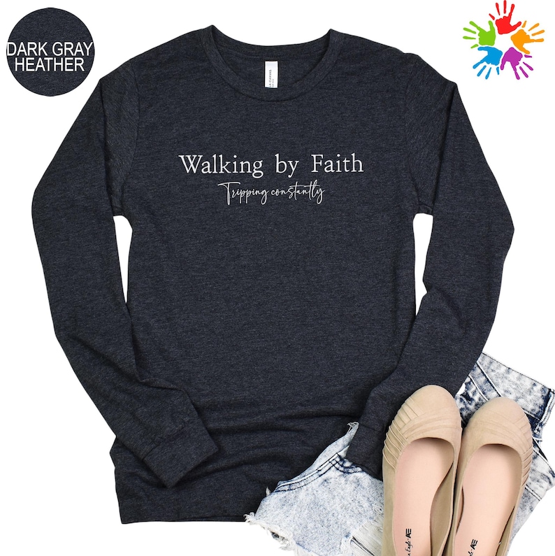 a dark gray long-sleeved shirt with the text "Walking by Faith" printed on it, along with a pair of beige shoes and a pair of denim shorts.