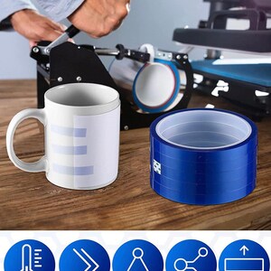 May include: A white ceramic mug with a light blue design, next to a roll of blue tape. The mug is on a wooden surface, with a heat press machine in the background. The tape is for sublimation, with features like short term instantaneous temperature, versatile uses, stable and reliable, not easy to break, and leave no residue.