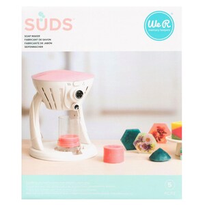 May include: A white and pink soap maker with the word "SUDS" in pink. The soap maker has a clear glass cylinder and a pink soap base. Several colorful, hexagonal soaps are displayed next to the soap maker.