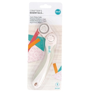 May include: An angled rotary cutter, packaged in a clear plastic sleeve. The cutter has a white handle with a light green accent and a silver blade. The packaging includes the text "CRAFTER'S ESSENTIALS" and "We R".