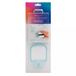 May include: A clear plastic package containing a ribbon and washi tape guide. The package has a gradient background of blue, pink, and purple. The text "PRINT MAKER" is visible, along with the words "RIBBON & WASHI GUIDE". A hand is shown using the guide.