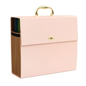 May include: A light pink expanding file folder with a gold-colored handle and clasp. The file folder has multiple interior pockets with colored dividers. The closed folder is rectangular and has a smooth surface.
