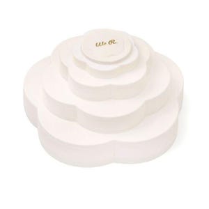 May include: A white, multi-tiered, flower-shaped paper craft with the text "We R." in gold lettering on the top tier. The craft has a layered design, with each tier slightly smaller than the one below.