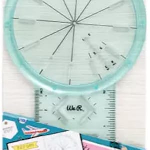 May include: A journal guide tool with a clear, circular design and a ruler. The packaging includes the text "JOURNAL GUIDE" in multiple languages and the brand name "We R". The image also shows journal pages.