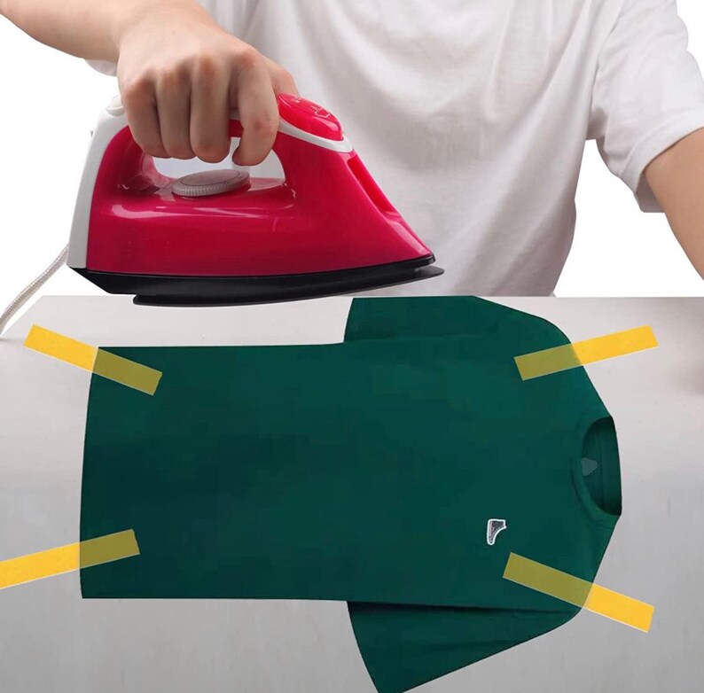 May include: A red and white iron being used on a folded dark green t-shirt. The t-shirt is secured with yellow tape. A small white logo is visible on the left chest area of the shirt. The person is wearing a white t-shirt.