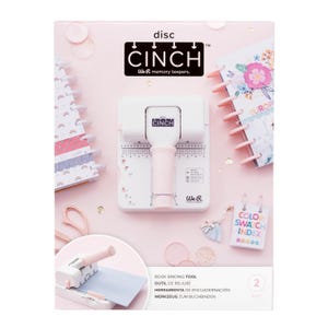 May include: A white Cinch disc binding tool with a pink handle, featuring the text "CINCH" and "We R memory keepers." The image includes a notebook, a color swatch index, and the text "BOOK BINDING TOOL".