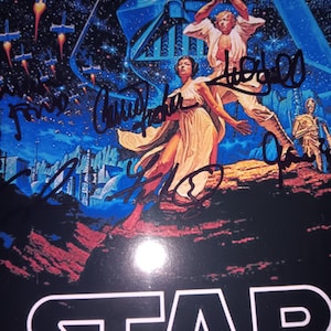 Może przedstawiać: Plakat filmowy Star Wars z Darthem Vaderem, Lukiem Skywalkerem, księżniczką Leią i C-3PO. Plakat ma niebiesko-czarne tło ze sceną bitwy kosmicznej. Słowo "STAR" znajduje się na dole. Plakat ma kilka podpisów.