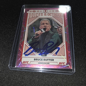May include: A pink holographic trading card featuring Bruce Buffer holding a microphone, labeled Voices of the Octagon. The card includes a blue ink autograph across the center, the text Bruce Buffer, and the UFC logo in a protective plastic case.