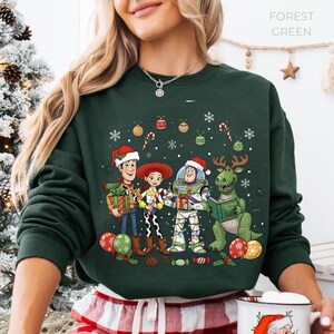 A woman wearing a green sweatshirt with a Christmas-themed graphic of characters from the Toy Story movie, including Woody, Buzz Lightyear, and a dinosaur.