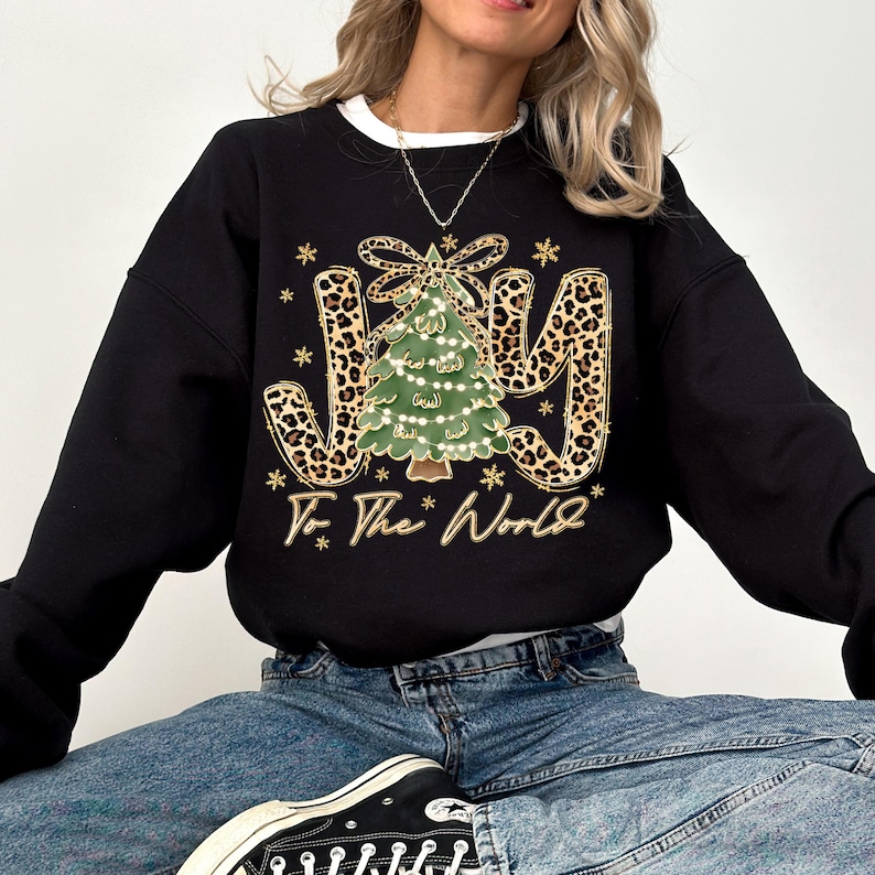 A woman wearing a black sweatshirt with a Christmas tree design and the text "To the World" printed on it.