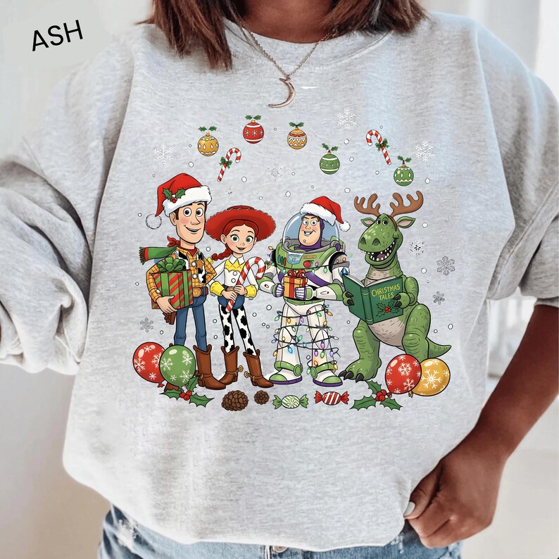 A person wearing a gray sweatshirt with a Christmas-themed graphic design featuring characters from the Toy Story franchise, including Woody, Buzz Lightyear, and a dinosaur.