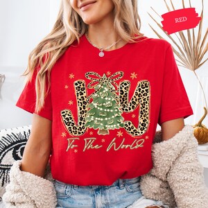 A woman wearing a red t-shirt with a Christmas tree design and the text "To the World" printed on it.