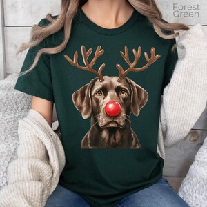 A woman wearing a green t-shirt with a brown dog wearing a red nose and antlers, which appears to be a Christmas-themed design.