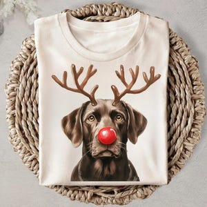 A white t-shirt with a printed image of a dog wearing a red nose and antlers, resembling a reindeer or Christmas character.