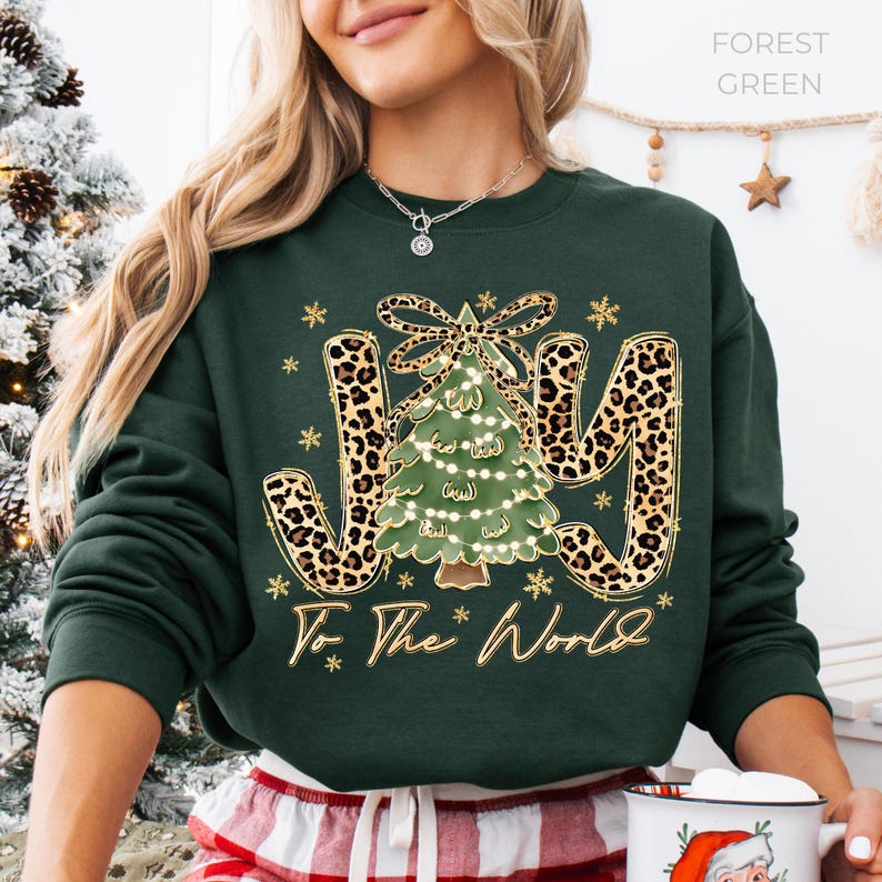 A woman wearing a green sweatshirt with a Christmas tree design and the text "Joy To The World" printed on it.