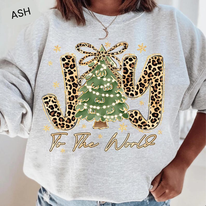 A person wearing a grey sweatshirt with a Christmas tree design and the text "Joy To The World" printed on it.