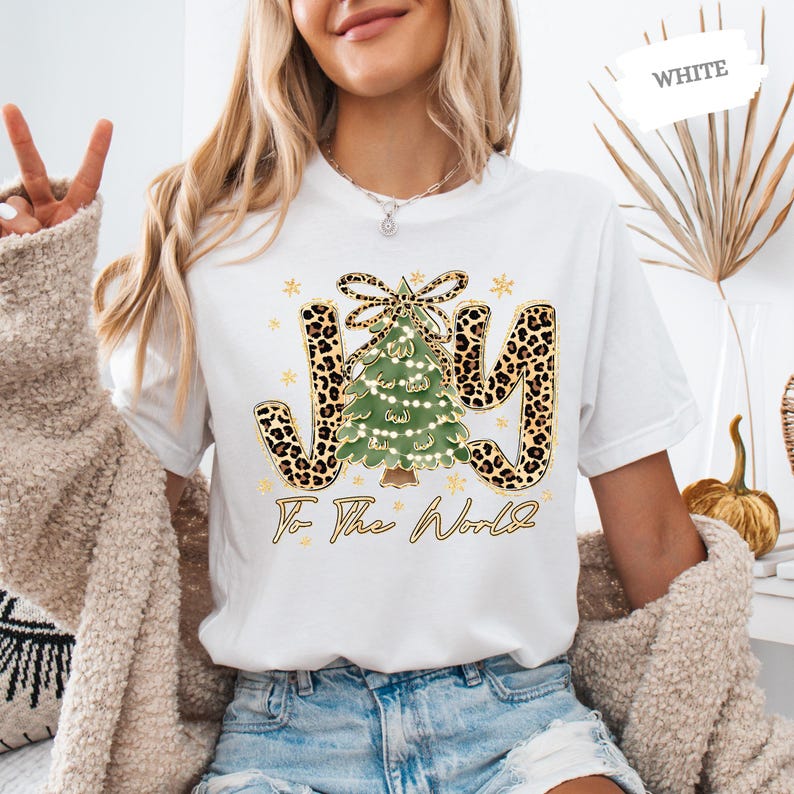 A woman wearing a white t-shirt with a Christmas tree design and the text "Joy To The World" printed on it.