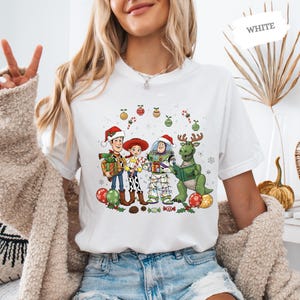 A woman wearing a white t-shirt with a cartoon illustration of characters from Toy Story, including Woody, Buzz Lightyear, and a dinosaur, along with Christmas decorations.