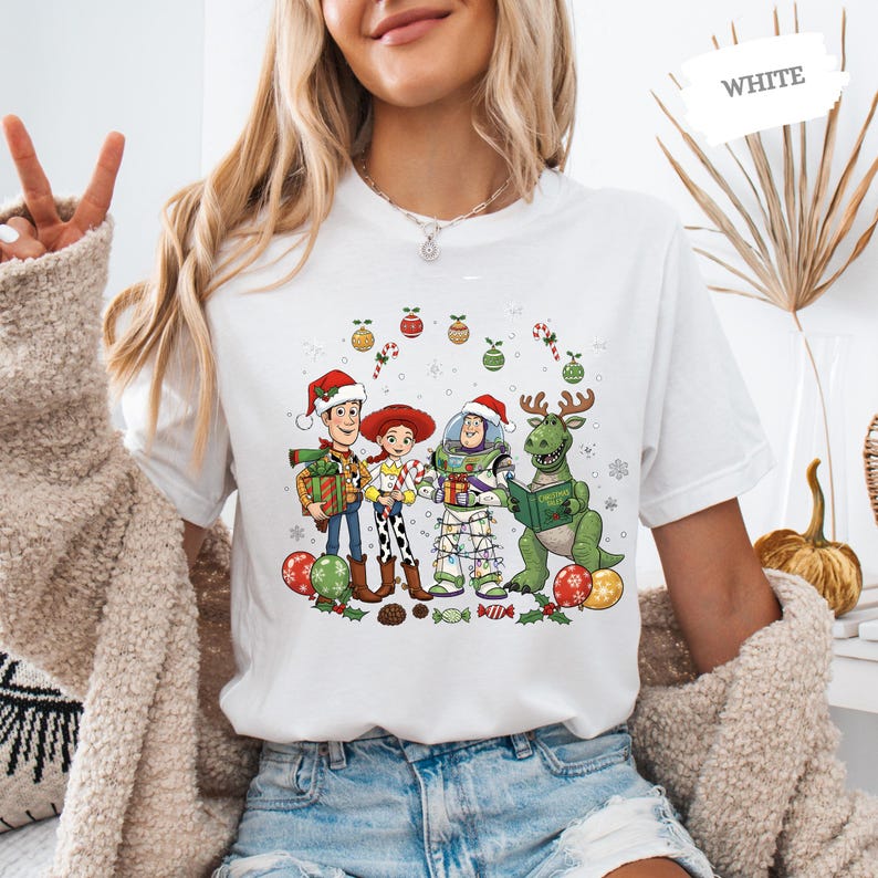 A woman wearing a white t-shirt with a cartoon illustration of characters from Toy Story, including Woody, Buzz Lightyear, and a dinosaur, along with Christmas decorations.
