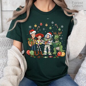 A green t-shirt with a Christmas-themed graphic design featuring characters from the Toy Story franchise, including Woody, Buzz Lightyear, and a dinosaur.