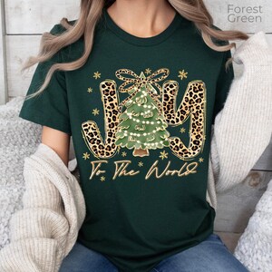 A woman wearing a green t-shirt with a Christmas tree design and the text "Joy To The World" printed on it.