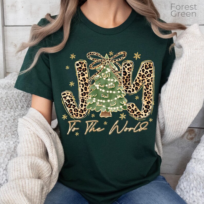 A woman wearing a green t-shirt with a Christmas tree design and the text "Joy To The World" printed on it.
