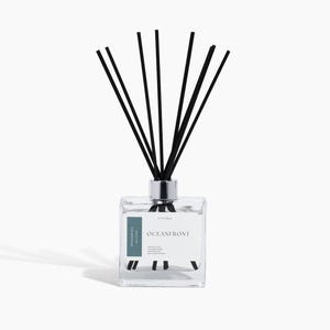 May include: A clear glass diffuser bottle with black reeds. The bottle has a silver cap and a label that reads "Oceanfront". The product is designed for home fragrance.