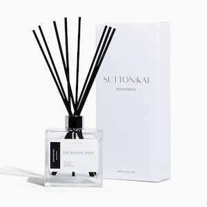 Peut inclure: Un diffuseur de roseaux en verre transparent avec des roseaux noirs et une boîte blanche. Le diffuseur a un bouchon noir et une étiquette qui dit "The Woodlands". La boîte blanche est étiquetée "Suttonkai Reed Diffuser Oil".
