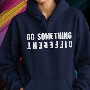 May include: A navy blue hooded sweatshirt featuring a front kangaroo pocket and long sleeves. The chest displays the white text DO SOMETHING with the word DIFFERENT printed directly below it in an inverted, upside-down orientation.