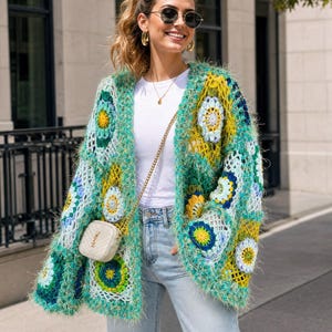 May include: A long-sleeved, open-front cardigan made of multi-colored crochet granny squares in shades of teal, lime green, yellow, and blue. The garment features a fuzzy, textured yarn finish and is worn over a plain white t-shirt and light blue jeans.