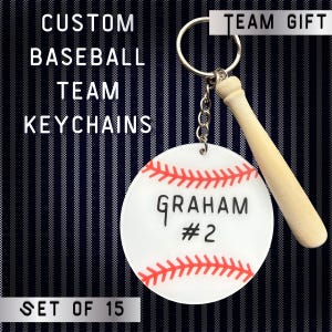 May include: A baseball-themed keychain with a white, red, and black design. The keychain features a baseball with red stitching, the name "GRAHAM" and the number "2". A small wooden baseball bat charm is attached to the keychain. The text "CUSTOM BASEBALL TEAM KEYCHAINS" is visible.