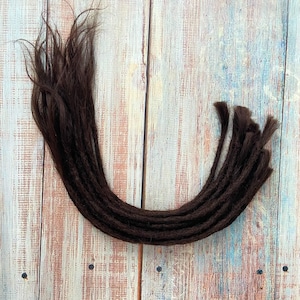 May include: Dark brown dreadlocks arranged in a curved shape. The dreadlocks are made of individual strands of hair, with a slightly textured appearance. The background is a light-colored wooden surface with blue and white accents.