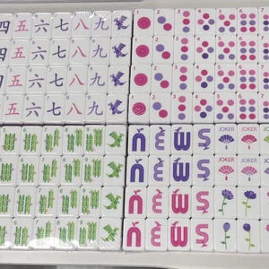 May include: A collection of white Mahjong tiles, each with unique symbols and characters in black, purple, and pink. The tiles feature numbers, bamboo, dots, and flower designs. Some tiles have the word "Joker".