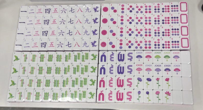 May include: A collection of white Mahjong tiles, each with unique symbols and characters in black, purple, and pink. The tiles feature numbers, bamboo, dots, and flower designs. Some tiles have the word "Joker".