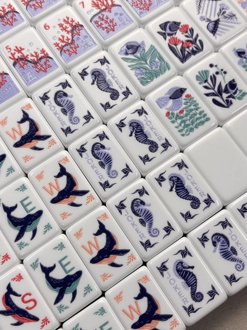 May include: White tiles with marine-themed illustrations, including seahorses, whales, and coral. Some tiles feature the word "JOKER" and numbers. The artwork is in shades of blue, orange, and red.