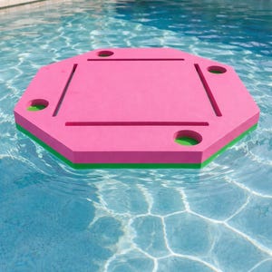 May include: A pink and green floating pool table with four cup holders and recessed areas. The octagonal table floats in a pool of clear blue water. The table is made of a foam material.