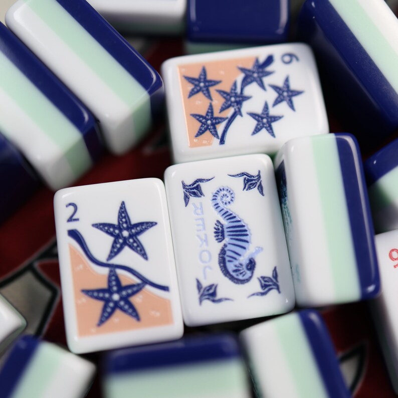 May include: Close-up of decorative tiles with a marine theme. The tiles feature starfish, seahorses, and the word "Joker" in blue. The tiles are white with blue, green, and orange accents. Some tiles have the number 2 or 6.