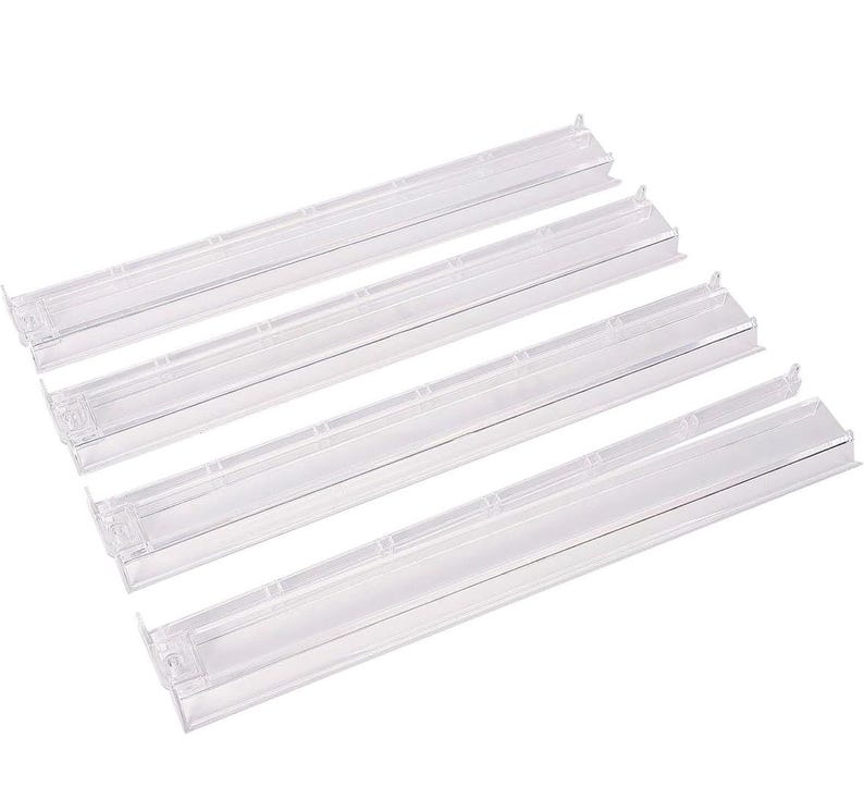 May include: Four clear, rectangular plastic shelf dividers with a long, narrow design. Each divider features a flat base and a vertical panel with small, protruding tabs along the top edge, designed for organizing items on a flat surface.