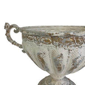 May include: A distressed white and gold decorative urn with a textured surface and ornate handles. The urn has a pedestal base and is suitable for indoor or outdoor use. The urn is approximately 12 inches tall.