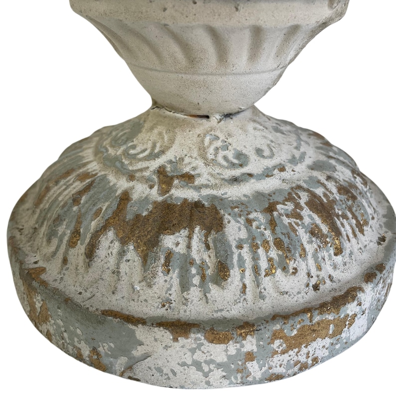 May include: Close-up of a distressed, off-white decorative pedestal with a round base. The base features gold and light blue accents, with a detailed, ornate design. The pedestal has a classic, vintage aesthetic.