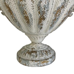May include: A distressed white and gold-accented urn with a fluted body and pedestal base. The aged finish gives the decorative planter a vintage aesthetic. The urn is suitable for indoor or outdoor use.