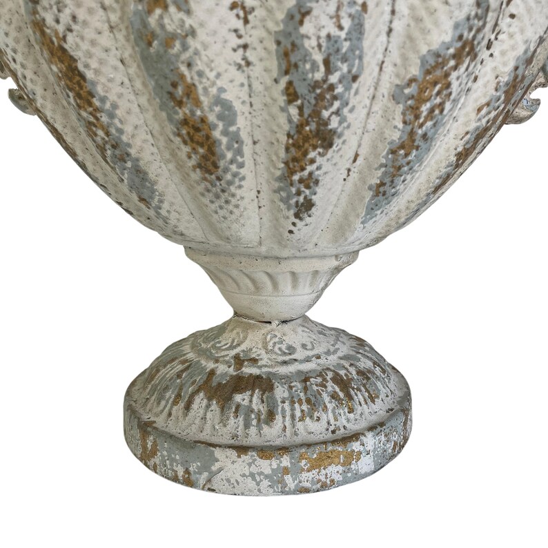 May include: A distressed white and gold-accented urn with a fluted body and pedestal base. The aged finish gives the decorative planter a vintage aesthetic. The urn is suitable for indoor or outdoor use.