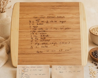 May include: A rectangular bamboo cutting board engraved with a handwritten recipe for Choc Chip Oatmeal Cookies. Two small paper cards featuring the same recipe are placed in front of the board, displaying ingredients and baking instructions.