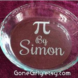 May include: Clear glass pie dish with the Greek letter Pi and the words "By Simon" etched on the bottom. The dish has two handles and is sitting on a dark purple surface. The Etsy shop name "GoneGirly.etsy.com" is visible.