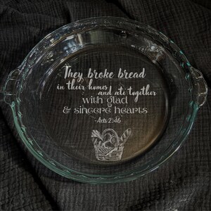 May include: Clear glass pie dish with etched text: "They broke bread in their homes and ate together with glad & sincere hearts - Acts 2:46." A basket of bread is also etched on the dish.
