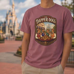 May include: A maroon t-shirt featuring a graphic of "The Dapper Dogs" with four cartoon figures enjoying hot dogs. The graphic includes the text "Casey's" and a castle in the background. The shirt is being worn by a person.
