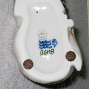 May include: White porcelain figurine with blue and green painted details. The figurine has a mark on the bottom that reads "Royal Copenhagen Denmark" and "2678".