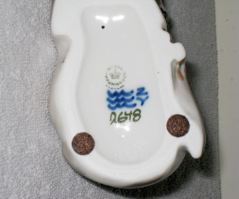 May include: White porcelain figurine with blue and green painted details. The figurine has a mark on the bottom that reads "Royal Copenhagen Denmark" and "2678".