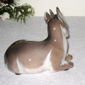 May include: A porcelain figurine of a fawn lying down. The fawn is brown and white with a glossy finish.